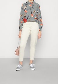 Blommig blus med grå bakgrund, vita skinny jeans och grå sneakers. Inkluderar en liten rosa handväska med kedjerygg.