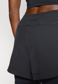 Pantalones cortos deportivos negros con tela ligera, cintura elástica y dobladillo curvado, con un bolsillo discreto en la parte trasera.