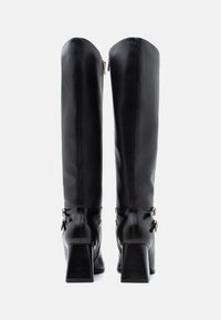 Μαύρες μπότες μέχρι το γόνατο με λείο δερμάτινο φινίρισμα, τετράγωνες ψηλές γόβες και διακοσμητικές πόρπες στο πλάι. Κλείσιμο με φερμουάρ στο πίσω μέρος.
