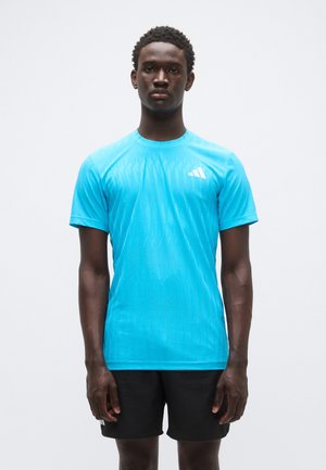 Lyseblå atletisk t-shirt med korte ærmer, med et tekstureret design og hvidt logo. Kombineret med sorte shorts.