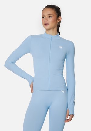 Light blue athletic jacket with a fitted design, high collar, and full-length sleeves. Features a zipper and logo detail on the chest.