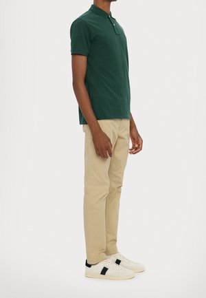 Grünes Baumwoll-Poloshirt mit Kragen, kombiniert mit beigefarbenen Chinos und weißen Sneakern mit schwarzen Details. Minimalistisches Design mit figurbetonter Passform.