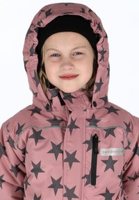 Roze winterjack met sterpatroon en kap, met grijze sterren, een ritssluiting aan de voorkant en een logo-opdruk op de borst. Zwarte gebreide beanie.