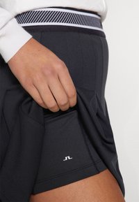 Svart sportskjol med texturerad midjeband som har randiga detaljer. En logotyp syns på tyget nära fållen. Slätt material.