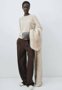 Beige gebreide trui, bruine op maat gemaakte broek en een lange, zachte, lichtbruine bontsjaal. Een grijze clutch en off-white schoenen maken de look compleet.