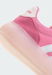 Růžové tenisky s texturovaným semišovým zadním dílem, hladkým syntetickým svrškem, bílými pruhy a průhlednou gumovou podešví. Logo vyšitá na patě.