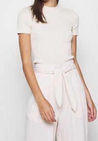 Haut à manches courtes en ribbed crème associé à un pantalon taille haute de couleur claire avec une ceinture à nouer et un tissu texturé.