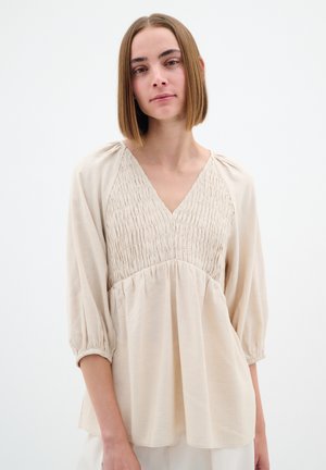 Blusa beige con scollo a V, corpetto arricciato e maniche a 3/4 leggermente imbottite. Realizzata in tessuto morbido con una vestibilità comoda e orlo arricciato.