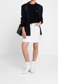 Czarny blezer, czarny sweter z logo, biała denimowa spódnica z postrzępionym dołem, białe botki na s�łupku oraz czarna torebka.