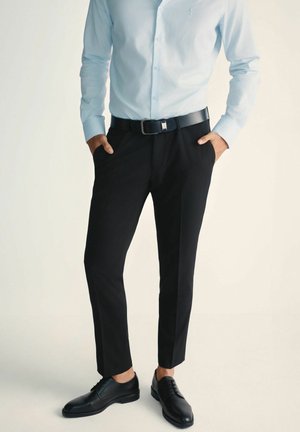 Jasnoniebieska koszula z guzikami, czarne dopasowane spodnie, czarny skórzany pasek i czarne buty eleganckie, podkreślające nowoczesny, smukły wygląd.