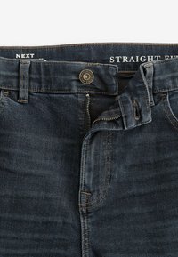 Tmavomodré džíny rovného strihu z denimu s uzatváraním na zips, mosadzným gombíkom a kontrastným prešívaním. Obsahujú päť vreciek.