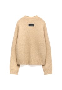 Pull en tricot beige au design court, avec des poignets et un ourlet côtelés, doté d'une étiquette noire dans le dos. Texture douce, coupe décontractée.