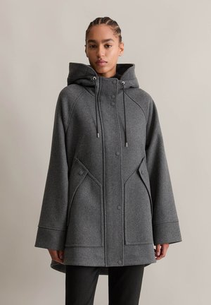 Cappotto grigio in misto lana con cappuccio, dotato di zip frontale, bottoni a pressione, tasche laterali e una vestibilità comoda. Dettagli di cucitura sulle maniche.