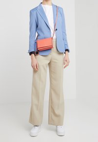 Blazer su misura azzurro chiaro sopra una maglietta bianca, abbinato a pantaloni beige a gamba larga e sneakers bianche. Inclusa anche una piccola borsa a tracolla arancione.