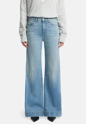Wijde jeans in lichtblauwe denim, met een hoge taille en een vervaagde afwerking, gecombineerd met een grijze top met lange mouwen en zwarte hakken.