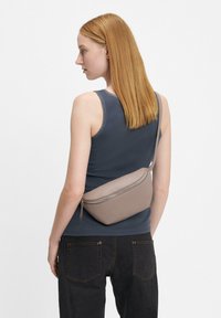 Brązowa nerka z sztucznej skóry z zamkiem, noszona na ciele. Czarne dżinsy ze złotymi przeszyciami oraz niebieski top na ramiączkach z koronkowym wykończeniem.