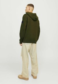 Olijfgroene hoodie met een gestructureerde afwerking, gecombineerd met lichtbeige, losse broek en beige laarzen. Minimalistisch ontwerp.
