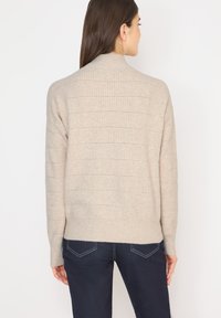 Beige neulepaita, jossa on ribbatut pinnan rakenteet ja va horizontal rinkulat. Kaulus on korkea ja istuvuus rento. Yhdistetty tummiin farkkuihin.