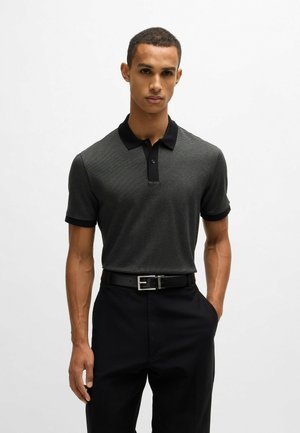 Polo noir à manches courtes avec un motif texturé, col noir et poignets noirs, associé à un pantalon noir et une ceinture à boucle en argent.