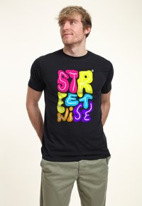 Camiseta negra con el texto multicolor "STREETWISE" en letras de burbuja en tonos de rosa, amarillo, azul, naranja y morado. Mangas cortas, cuello redondo.