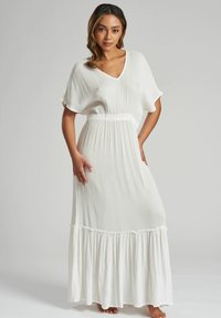 Robe maxi blanche avec un décolleté en V et des manches courtes et larges. Dotée d'une taille froncée et d'un ourlet à volants, fabriquée en tissu léger et texturé.