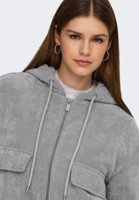 Hall triiksärk-tangidega kapuutsi, esikinnitusel tõmblukk ja kaks taskut. Näitab soonilist tekstuuri ja kontrastseid paelu.