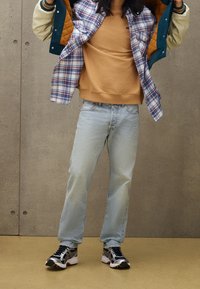 Outfit casual con un maglione beige, una giacca a quadri blu con bottoni, jeans azzurri chiari e scarpe da ginnastica nere e argentate.