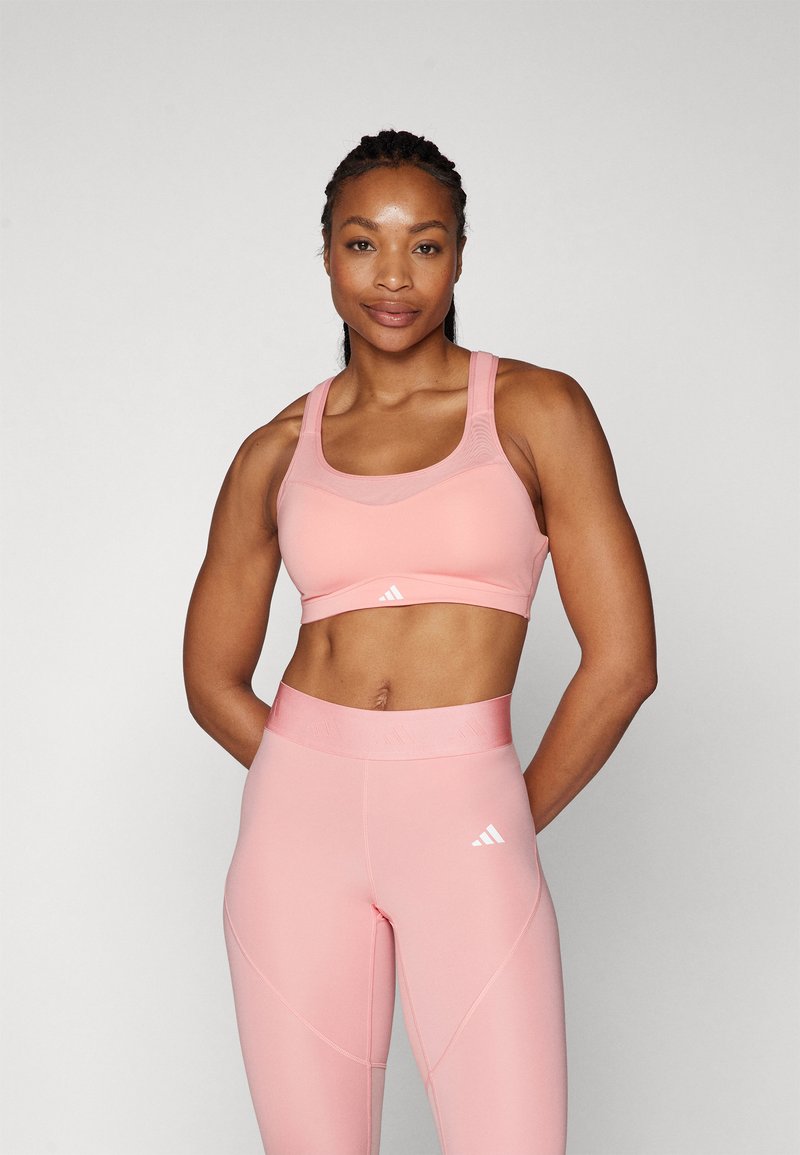 Bra sportivo rosa con bretelle larghe e scollatura a girocollo, abbinato a leggins a vita alta in tinta unita con una vita texturizzata e un dettaglio con logo.