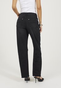 Jeans neri a vita alta con vestibilità rilassata, design a cinque tasche, texture sbiadita, orlo sfilacciato e dettagli in metallo color argento.