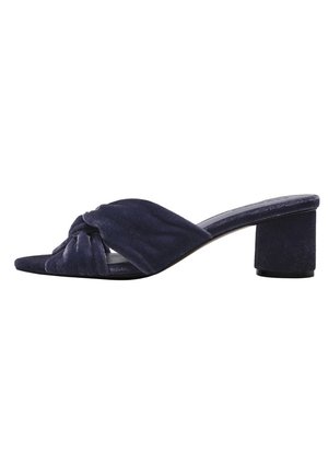 Mules à talons en suede bleu marine avec un bandeau avant tordu et un talon bloc. L'empeigne est légèrement rembourrée pour le confort et le style.