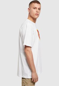 White cotton t-shirt with short sleeves, featuring a yellow and red logo design on the chest. Loose fit and round neckline.