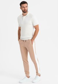 Vit rutig polo skjorta med krage, kombinerad med beige tapered byxor med vita sidostråk och vita sneakers.