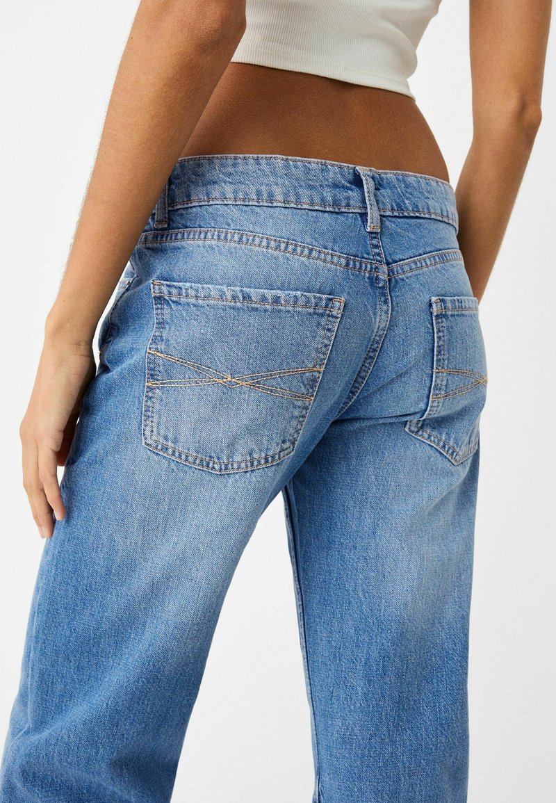 Los jeans de mezclilla azul claro presentan una cintura alta, un diseño de pierna recta y dos bolsillos traseros con costuras decorativas. Tejido suave y texturizado.