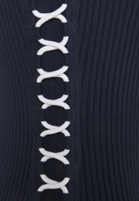 Granatowy sweter z prążkowanego dzianiny, z białymi sznurkami wzdłuż środka, z pętlami i krzyżującymi się wzorami, które nadają wizualną teksturę.