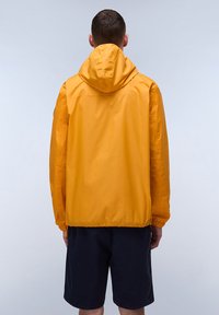 Yellow lightweight jacket with a hood, elastic cuffs, and a slightly textured finish, worn with dark shorts, viewed from the back.