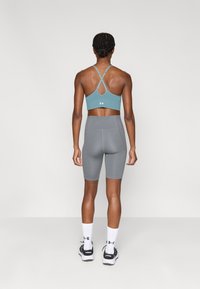 Ανοιχτό γαλάζιο αθλητικό σουτιέν με σταυρωτή πλάτη, σε συνδυασμό με γκρι σορτς ποδηλασίας ψηλόμεσα. Το μοντέλο φορεί λευκές κάλτσες και μαύρα αθλητικά παπούτσια.