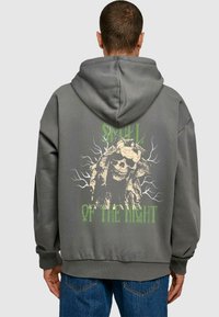 Felpa grigia con cappuccio caratterizzata da una grande grafica di teschio e testo verde che recita "SMULL OF THE NIGHT" con design simili ad alberi. Tessuto morbido e vestibilità rilassata.