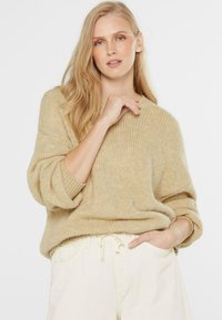 Beige Strickpullover mit lässiger Passform, gerippten Bündchen und rundem Halsausschnitt. Kombiniert mit hellen Trousers mit Kordelzug.
