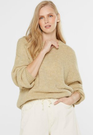 Beige Strickpullover mit lässiger Passform, gerippten Bündchen und rundem Halsausschnitt. Kombiniert mit hellen Trousers mit Kordelzug.