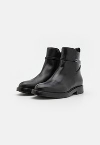 Black leather ankle boots with a smooth finish, round toe, short shaft, zipper closure, and a decorative strap with a silver accent.