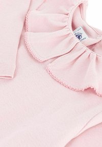 Helles rosa Langarmshirt mit einem gerüschten Kragen und gewellten Kanten aus weichem, glattem Stoff. Etikett sichtbar im Halsausschnitt.