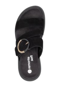 Black slip-on sandal with overlapping soft fabric straps, featuring a circular gold and black buckle accent, cushioned insole, and rounded toe.
