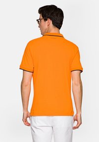 Pomarańczowa koszulka polo z kontrastowym czarnym wykończeniem na kołnierzyku i rękawach. Posiada krótkie rękawy i klasyczny krój.