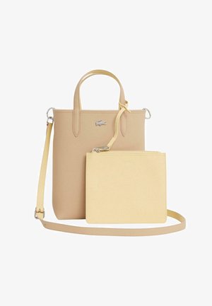 Beige rektangulær shopper med top-håndtag og aftagelig skulderrem, kombineret med en mindre lysegul håndledspung fastgjort foran.