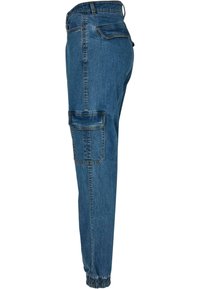 Pantalon cargo en jean bleu avec poche à rabat latérale, poche arrière, passants pour ceinture et poignets élastiqués, vu de côté.