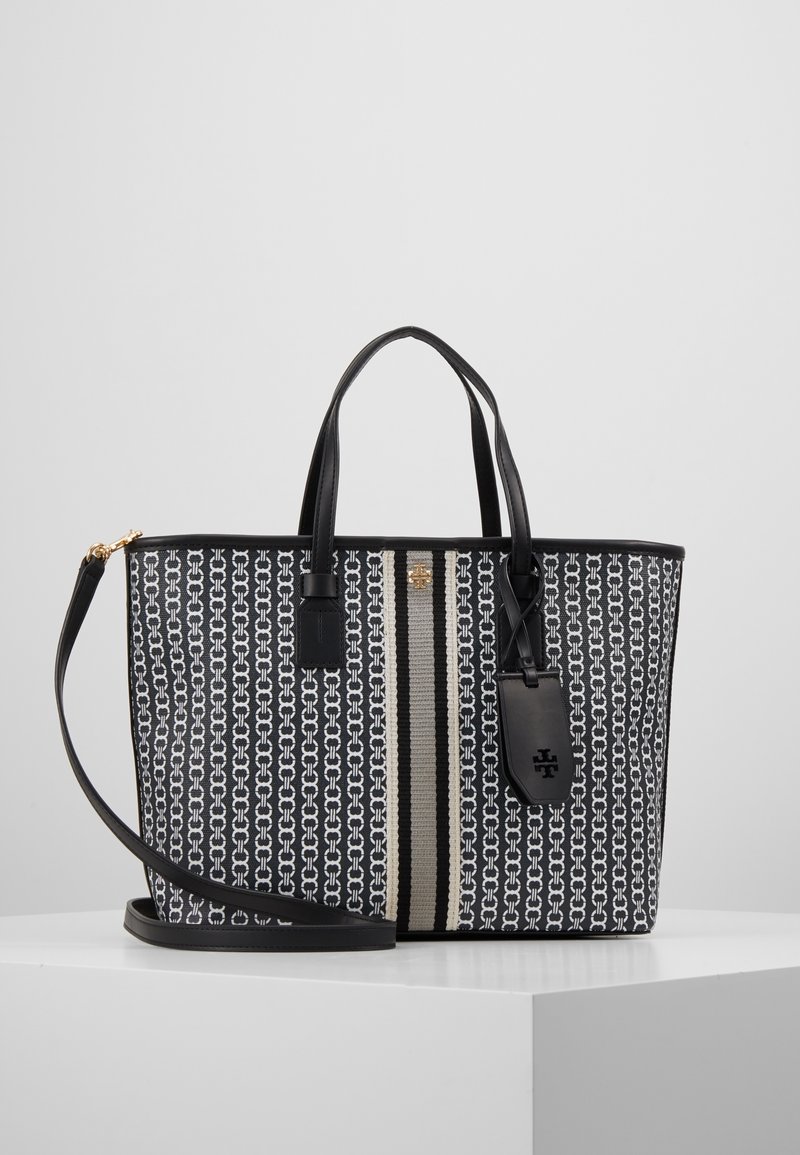Sac cabas à motifs noir et blanc avec deux poignées, une bandoulière amovible, un détail rayé vertical et une étiquette noire suspendue.