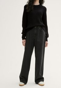 Pull noir à côtes avec manches longues, associé à un pantalon en denim gris foncé à taille haute et jambes larges, et des baskets blanches avec des accents beige.