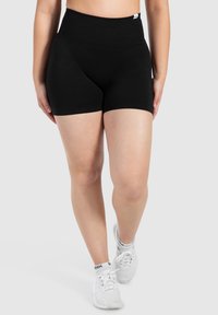 Zwarte gebreide shorts met een hoge tailleband. Heeft een gladde textuur en een aansluitend ontwerp. Gecombineerd met witte sportschoenen.