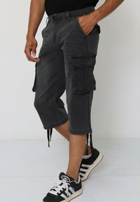 Shorts cargo gris avec de multiples poches, une coupe décontractée et un ourlet à la cheville avec des cordons de serrage. Associés à des chaussures de sport noires.