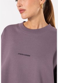 Felpa viola con colletto a girocollo rigato e tessuto texturizzato. Logo "PEGADOR" in lettere scure centrato sul petto.
